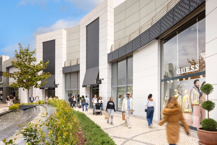People walking by modern shops with large windows on a sunny day.