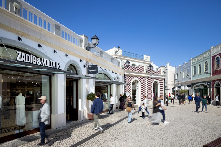 Outdoor shopping street with people walking and store facades.