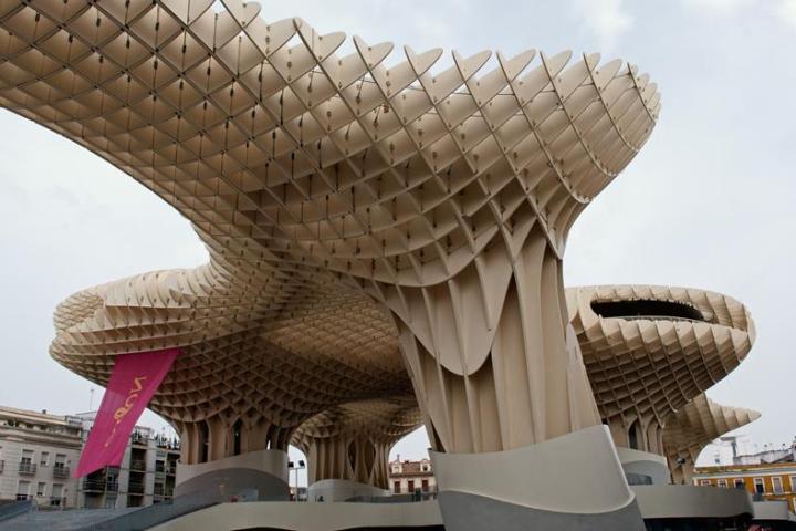 a bird sitting on top of a chair with Metropol Parasol in the background