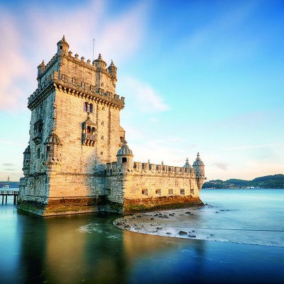 a large clock tower sitting in the water with Belém Tower in the background