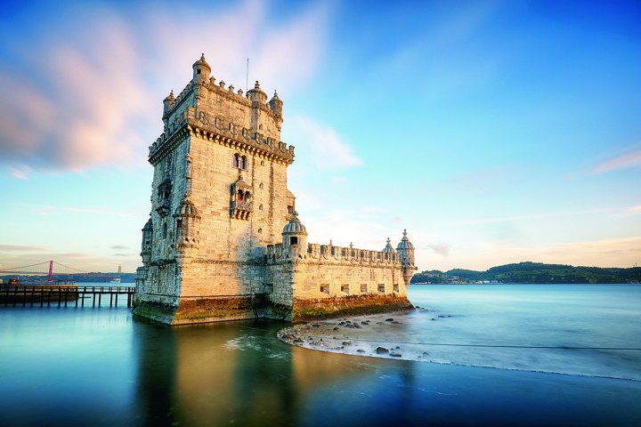 a large clock tower sitting in the water with Belém Tower in the background