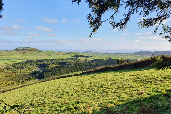 Scenic view of rolling green hills and distant mountains under a blue sky with clouds.