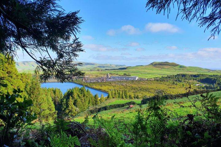 Scenic view of green hills, trees, and a lake under a blue sky with light clouds.