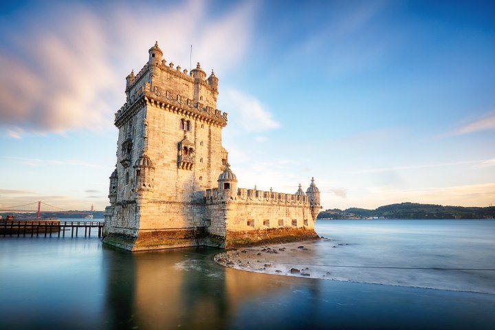 a castle with a clock tower in front of water with Belém Tower in the background