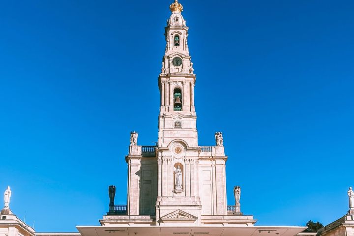 Tall white cathedral with statues and a cross, under a clear blue sky.