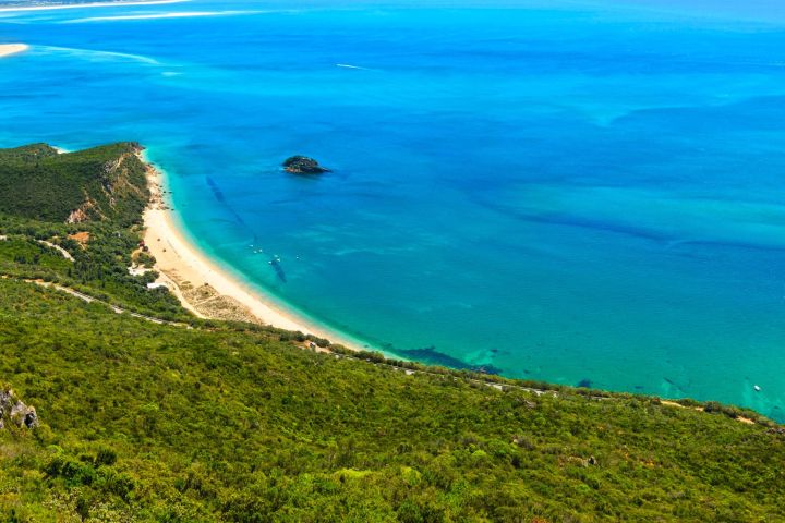 Aerial view of a green coastline and blue sea with a small island.