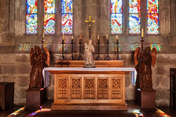 Church altar with crucifix, statues, and colorful stained glass windows.