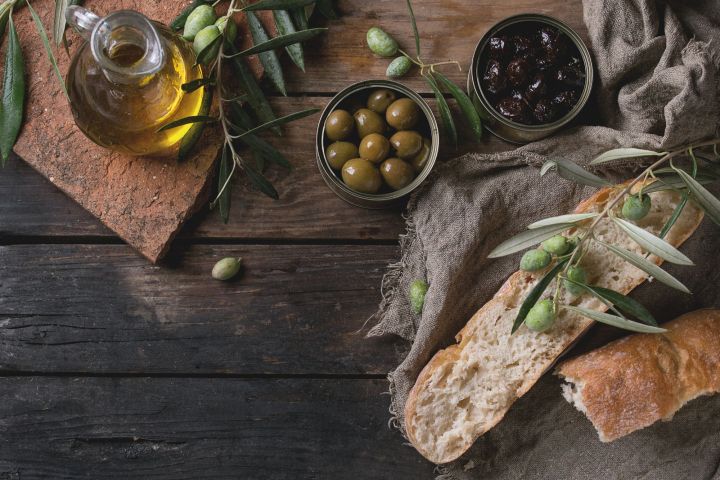 Rustic setup with olive oil, green and black olives, bread, and olive branches on a wooden table.