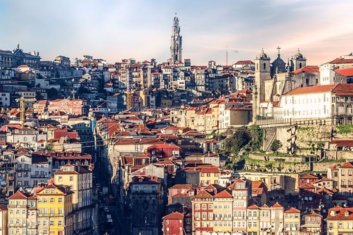 Hilly cityscape with colorful buildings and a tall tower under a blue sky.