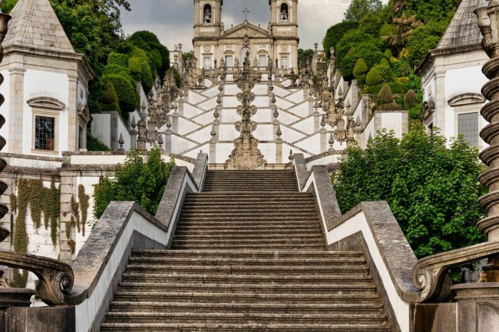 Grand staircase leading to a historical church with cloudy sky and lush greenery.