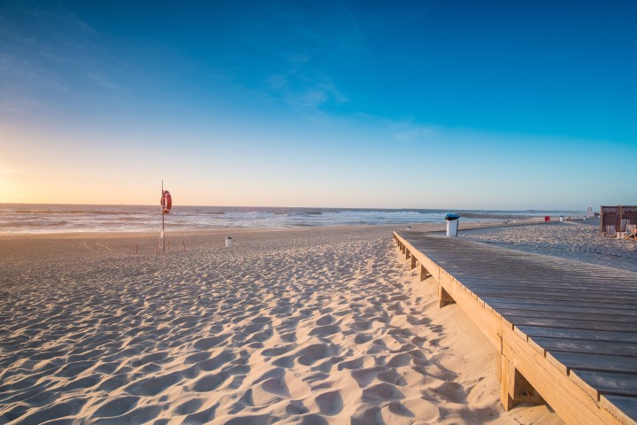 Wooden boardwalk on a sandy beach with a life buoy and clear blue sky.