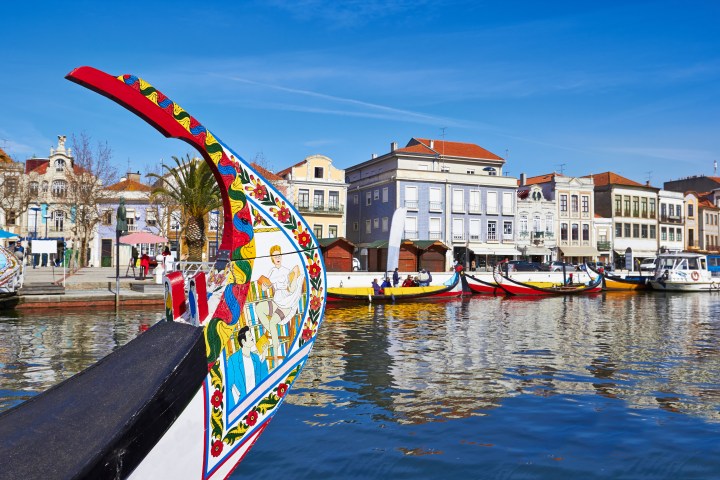 Colorful gondolas on a canal with historic buildings and palm tree, under a clear blue sky.