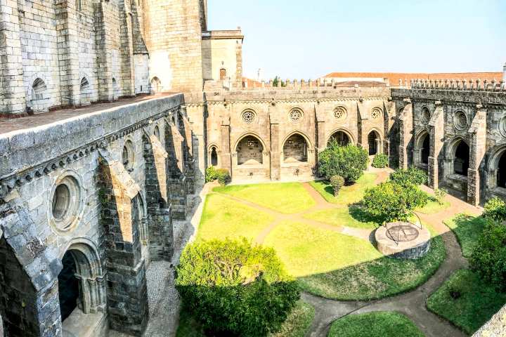 Historic stone courtyard with arches, circular windows, and garden paths.