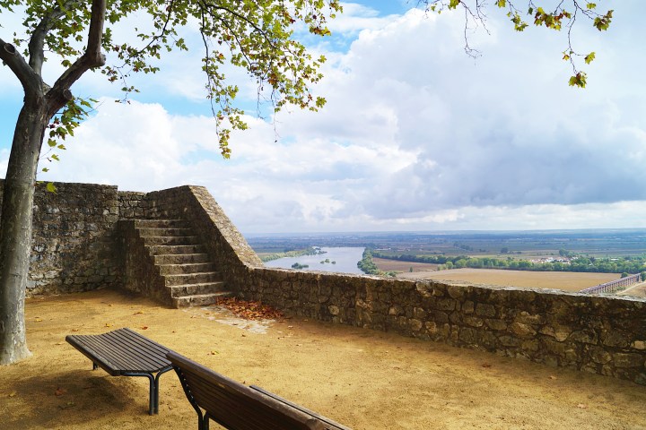 Stone steps and bench by a tree overlooking a river valley under a cloudy sky.