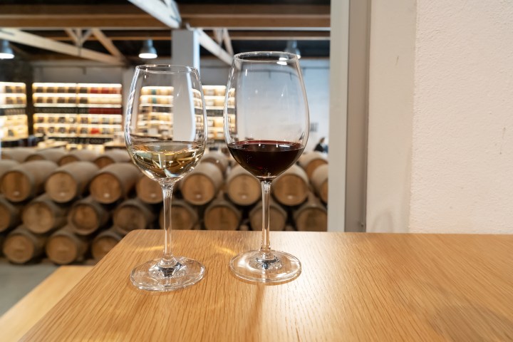 Two wine glasses, one with white and one with red wine, in a barrel room.