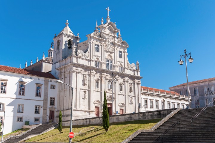 Baroque-style church with ornate facade under clear blue sky, steps and lampposts in foreground.