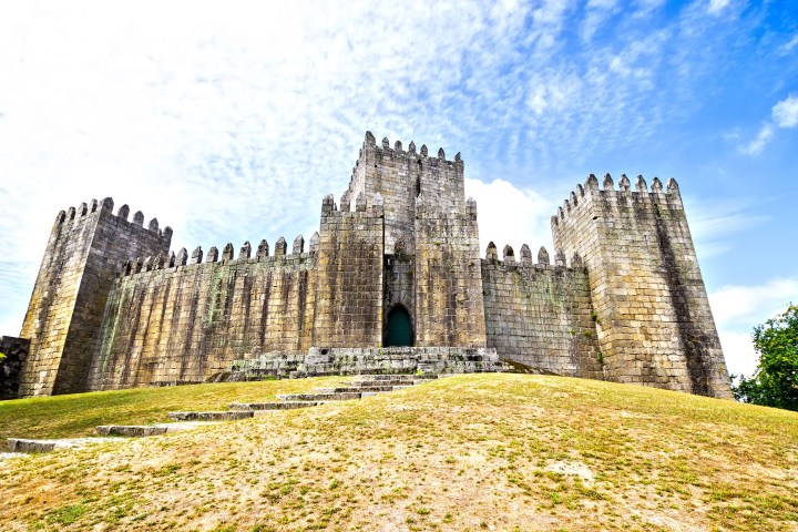 Stone castle with battlements under a cloudy blue sky.