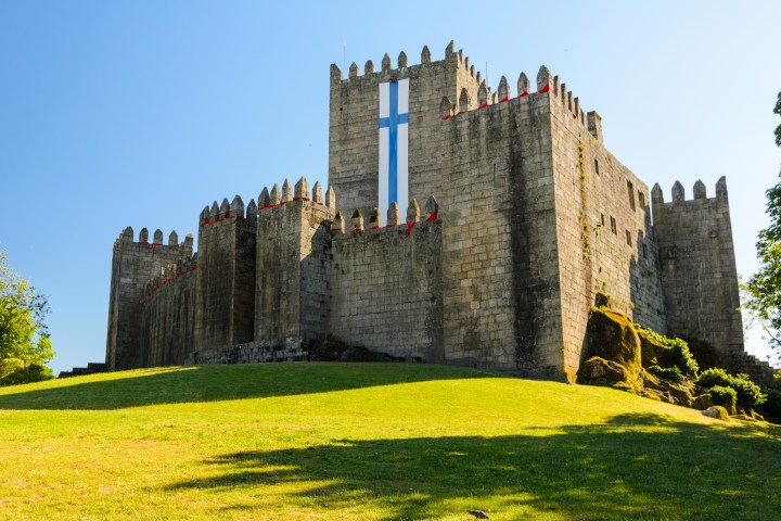 Stone castle with crenellations and large vertical banner on a sunny day.