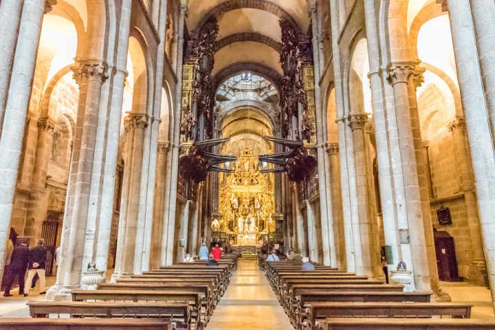 Interior of ornate cathedral with tall arches and golden altar at the end of the aisle.