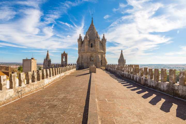 Stone rooftop with crenellations and tower under a blue sky with scattered clouds.