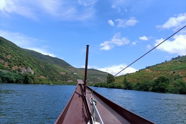 Boat's bow on a river with green hills and blue sky in the background.