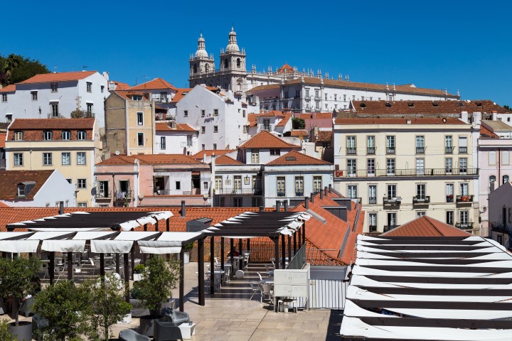 Rooftop view of Lisbon with colorful buildings and church towers under a clear blue sky.