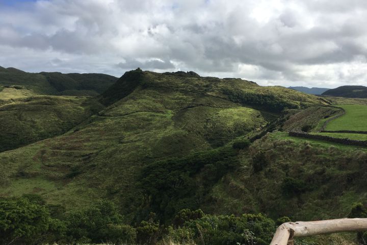 Hilly landscape with green grass, rocky terrain, and cloudy sky.