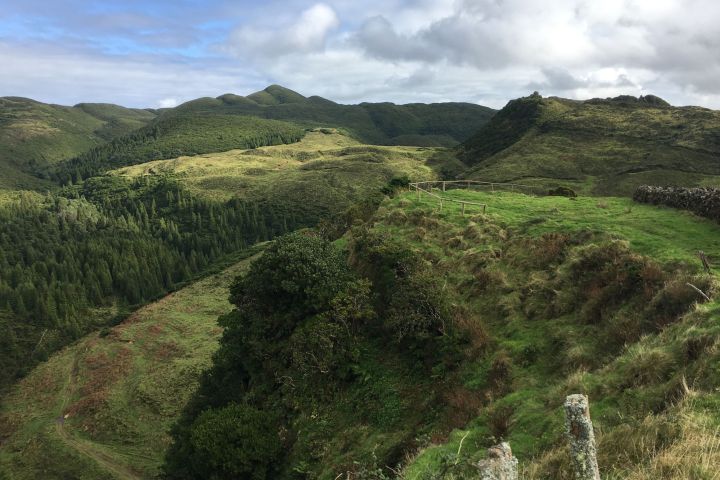 Lush green hills with a pathway and cloudy sky in the background.