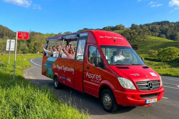 Red sightseeing bus with tourists on a scenic road near green hills.