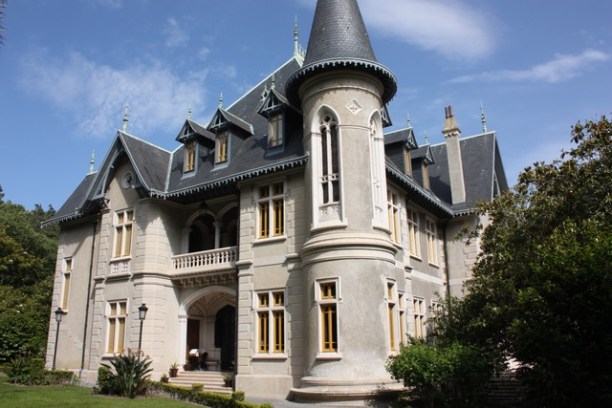 Gothic-style mansion with turret, steep roof, and multiple windows against a blue sky.