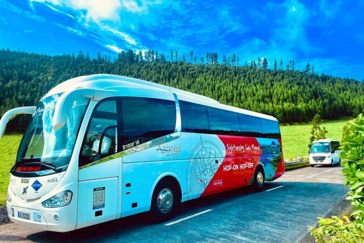 Tour bus parked on a road with green hills and blue sky in the background.