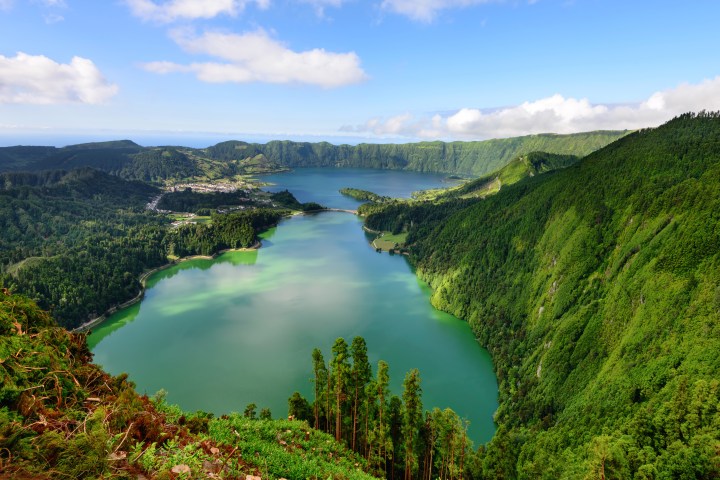 Scenic view of twin green lakes surrounded by lush hills under a blue sky with white clouds.