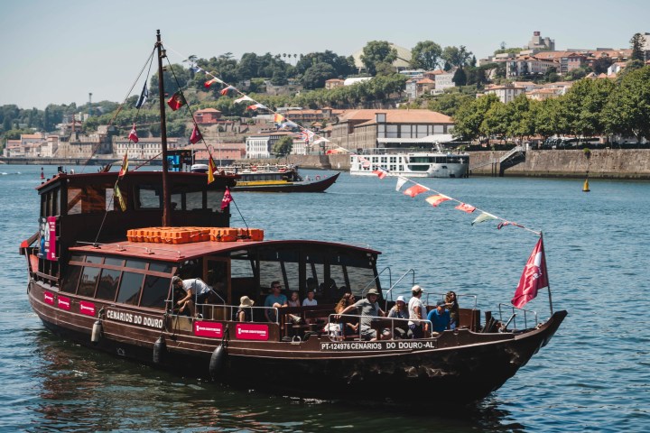 Tour boat on a river with colorful flags and scenic city background on a sunny day.