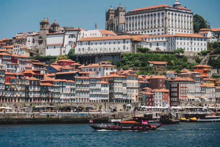 Colorful hillside buildings in Porto, Portugal, with boats on the Douro River under a clear blue sky.