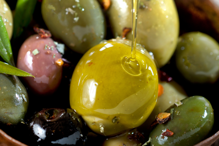 Close-up of assorted marinated olives with herbs drizzled in oil in a bowl.