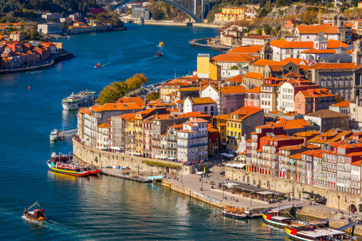 Colorful riverside buildings and boats on waterfront with bridge in the background under a clear blue sky.