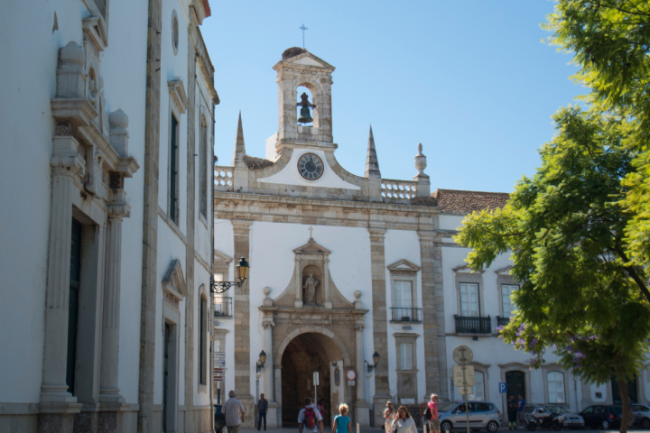 People walking towards a historic building with a bell tower on a sunny day.