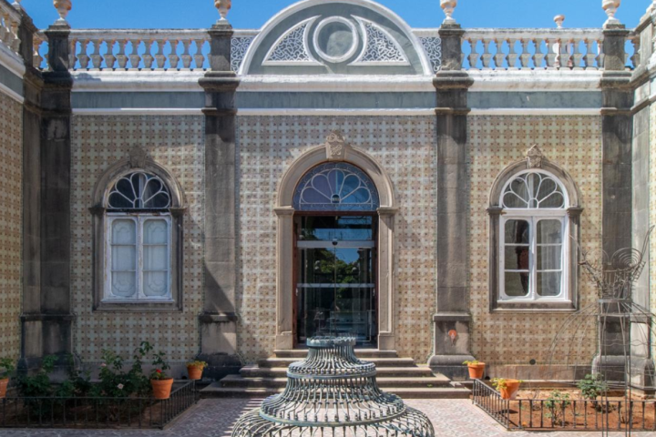 Ornate building facade with arched windows and decorative patterns, featuring a metal sculpture in the foreground.