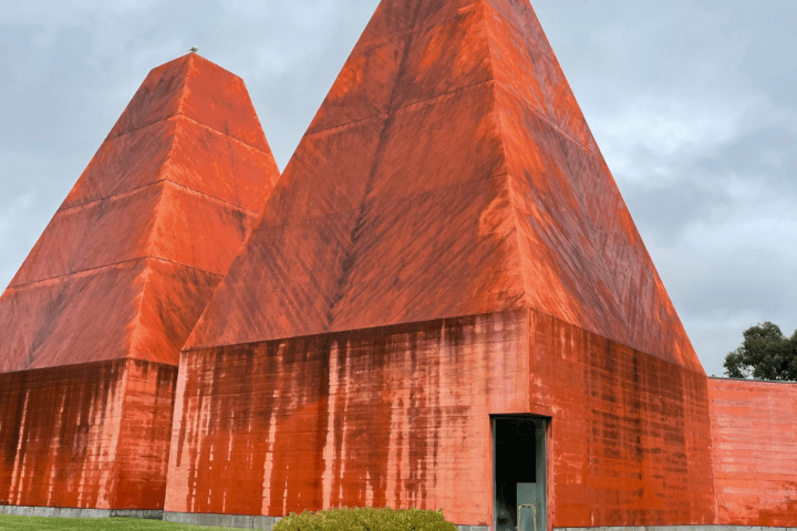 Two large orange pyramid-shaped buildings with a small tree in front, set against a cloudy sky.