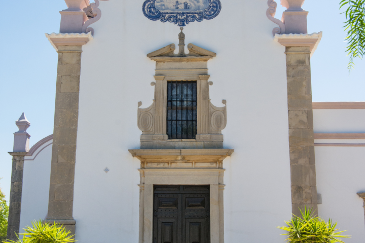 Ornate white church facade with stone columns, central door, and blue tile artwork above.