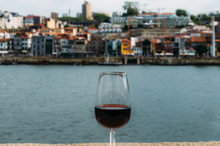 Wine glass on table with river and cityscape in the background.
