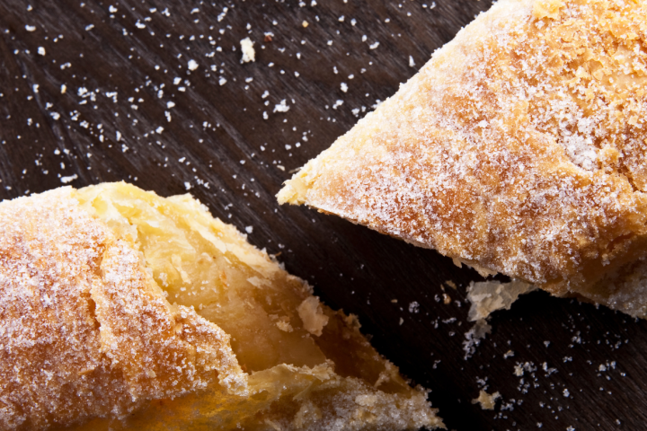 Two sugar-dusted pastry pieces on a dark wooden surface.
