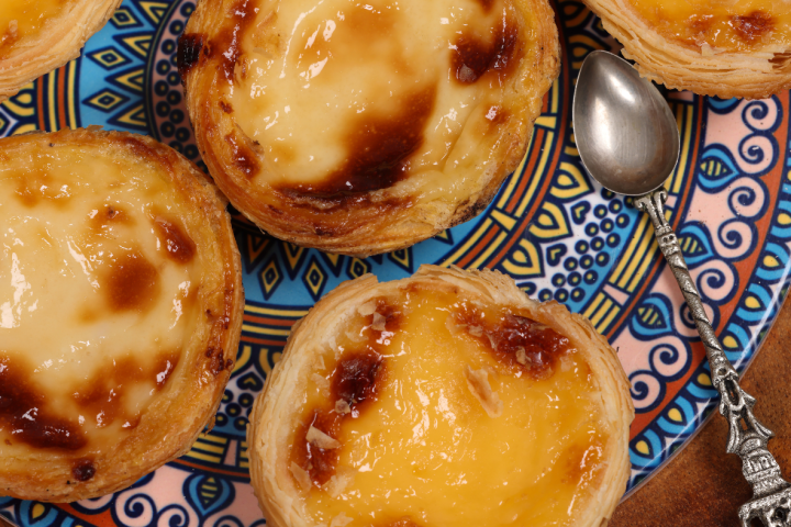Top view of five custard tarts on a patterned plate with a decorative spoon.
