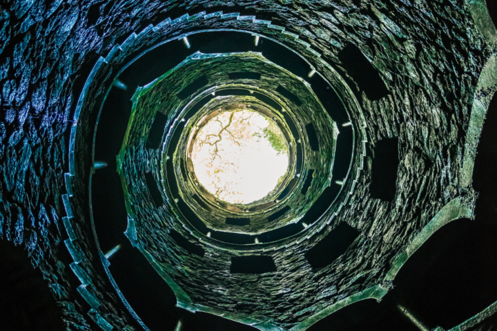 View looking up a spiral stone staircase with a bright opening at the top.