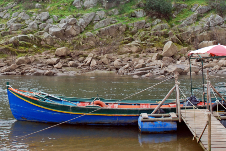 Colorful boat moored to a wooden pier by a rocky riverbank.