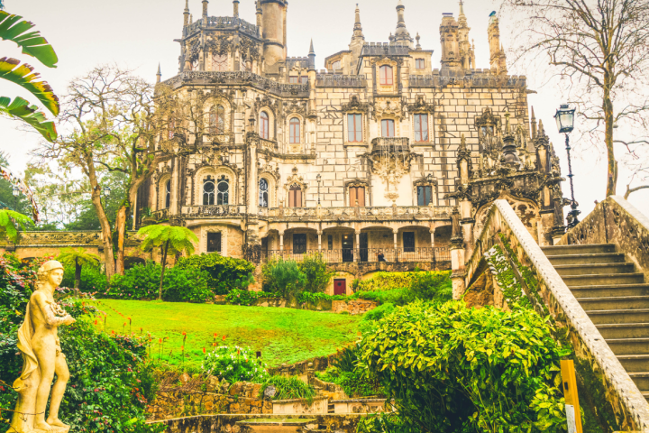 Ornate stone building with towers, surrounded by lush gardens and statues.