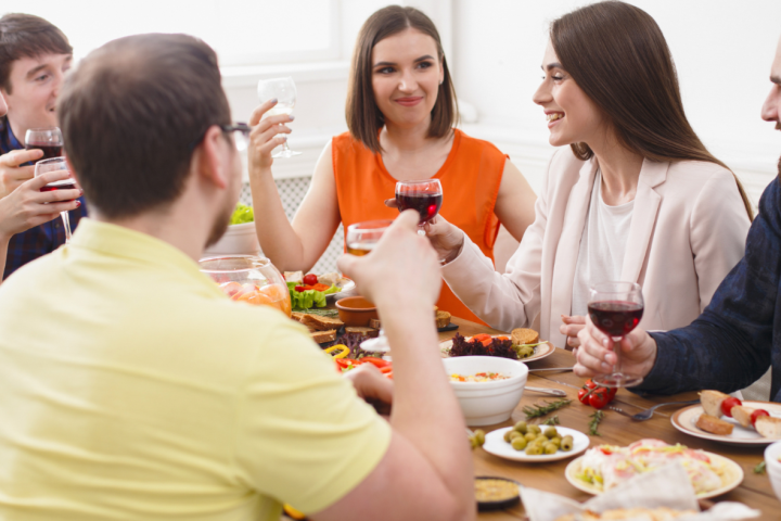 Group of people toasting with wine glasses around a table with food dishes.