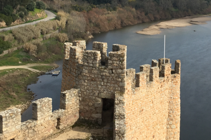 Stone castle tower overlooking a river with distant trees and a winding road.