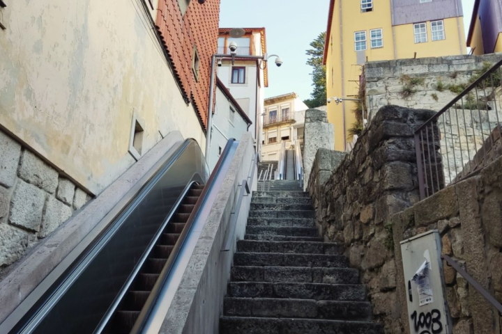 Stone staircase and escalator between buildings under a clear sky.