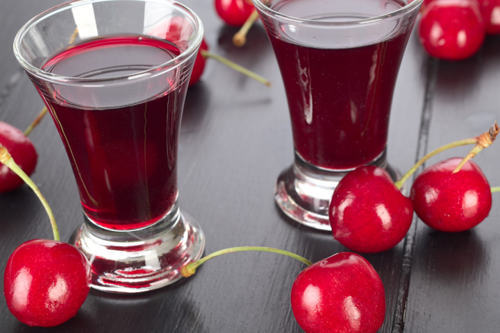Two glasses of cherry juice with fresh cherries on a black wooden table.